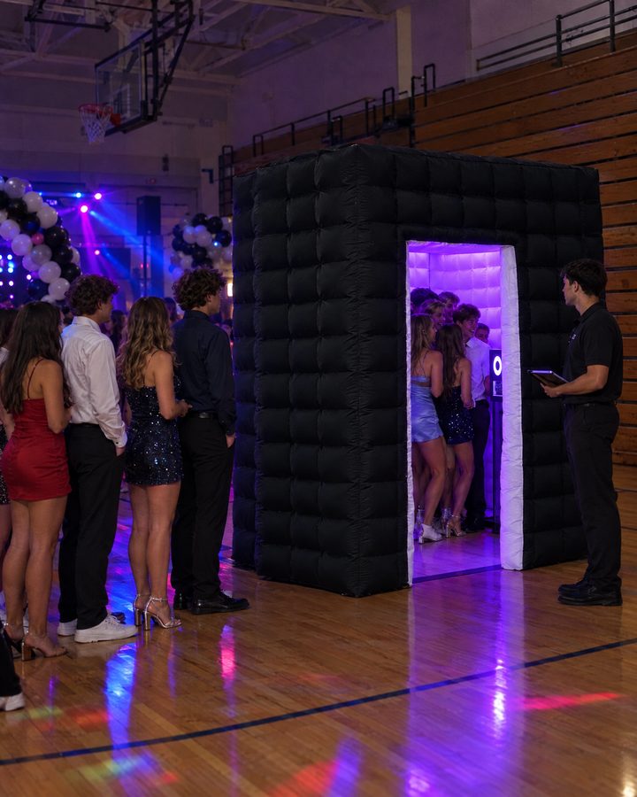 An AI-generated image of teenagers in homecoming outfits crowding into the black Flash Haus, glowing purple inside, at a dance in a school gym