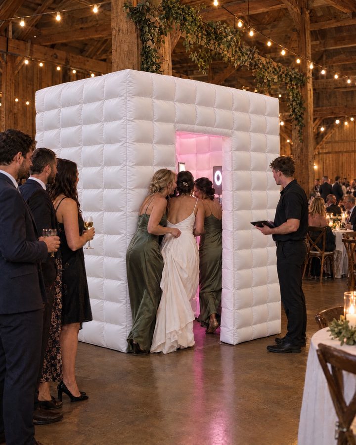 An AI-generated image of a bride and her bridesmaids stepping into the white Flash Haus, glowing soft pink inside, at a barn wedding reception