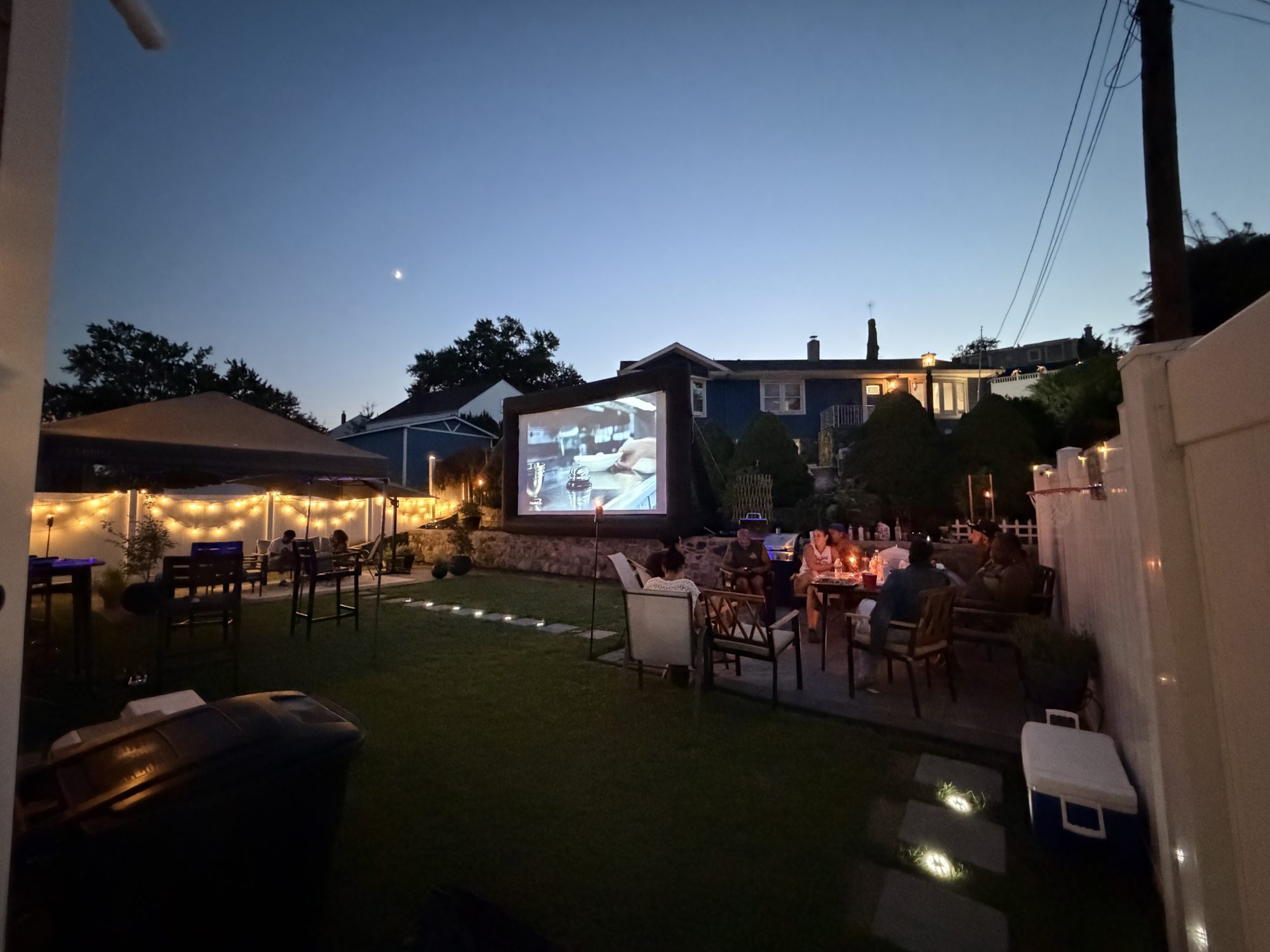 The Light Haus backyard movie night: guests watching an inflatable screen under string lights at dusk