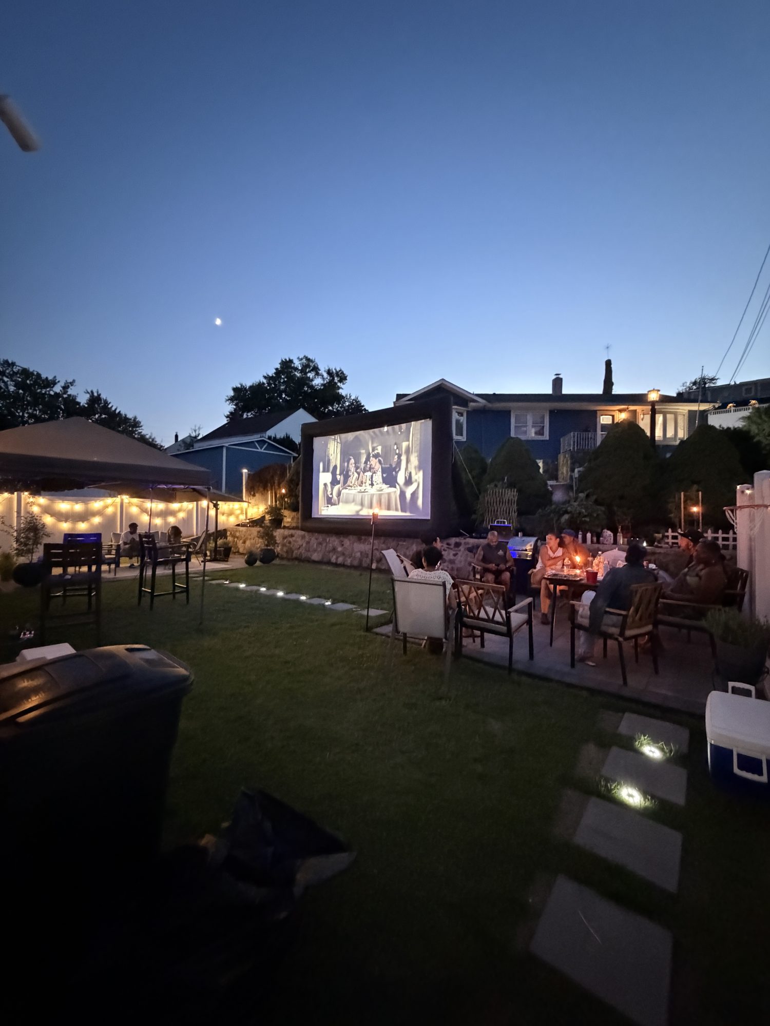 The Light Haus screen set up on a lawn at dusk with guests seated in front of it